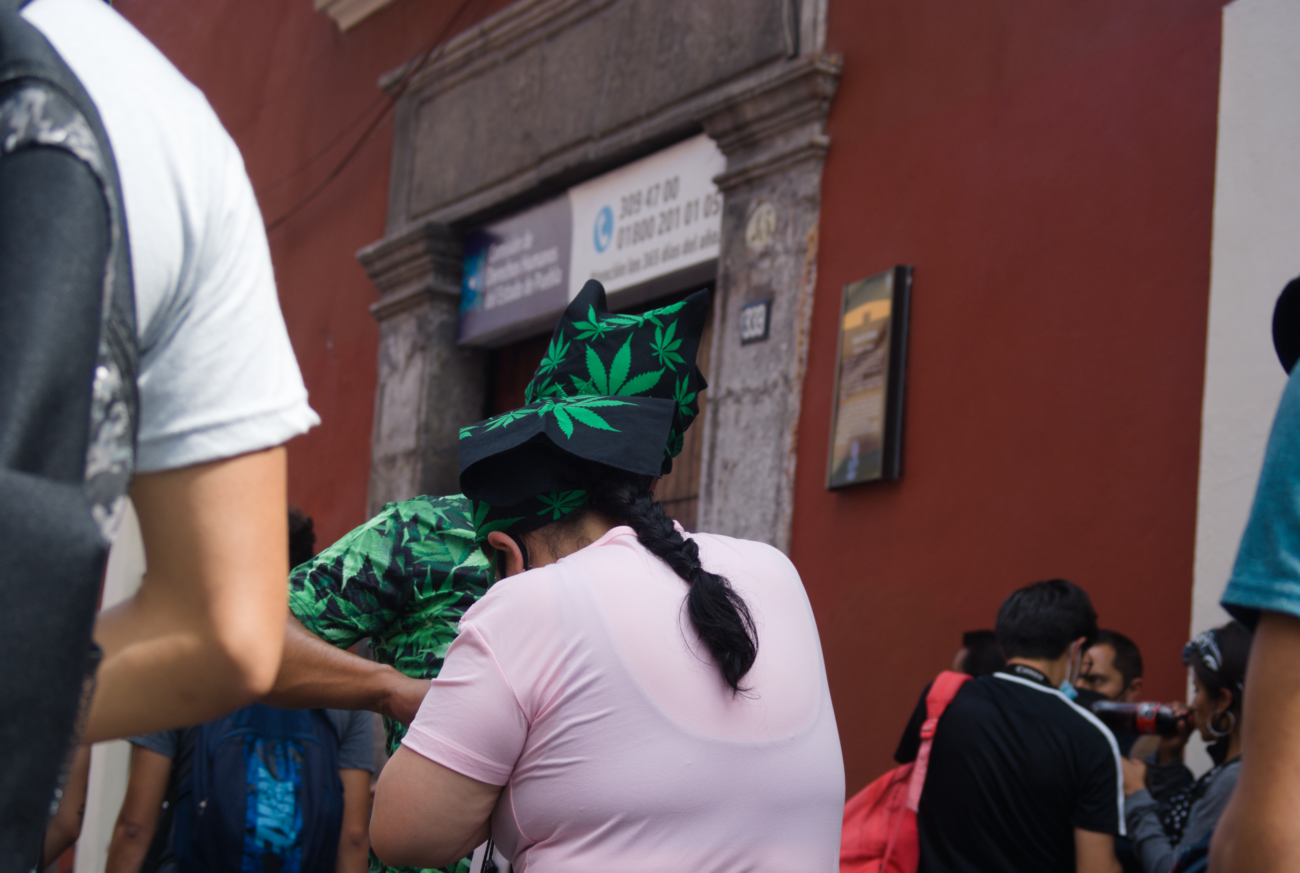 Una pareja con sombreros que tienen motivos de hojas de cannabis, celebran el 4:20 a las afueras de la Comision de Derechos Humanos de Puebla.